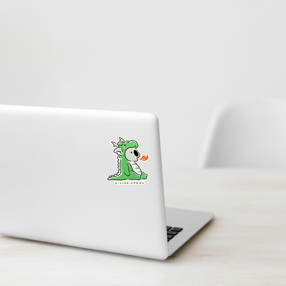 Cute Koala in Dragon Costume ✦ B-Side Label Sticker shown on a white laptop; illustrative placement, not to scale.